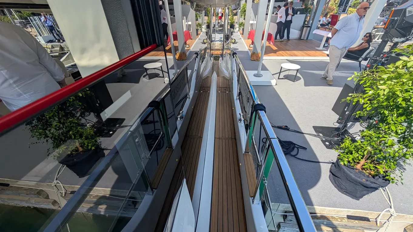 Aerial view of a luxurious yacht walkway, featuring wooden decking, reflections, and event setup with guests in the background.